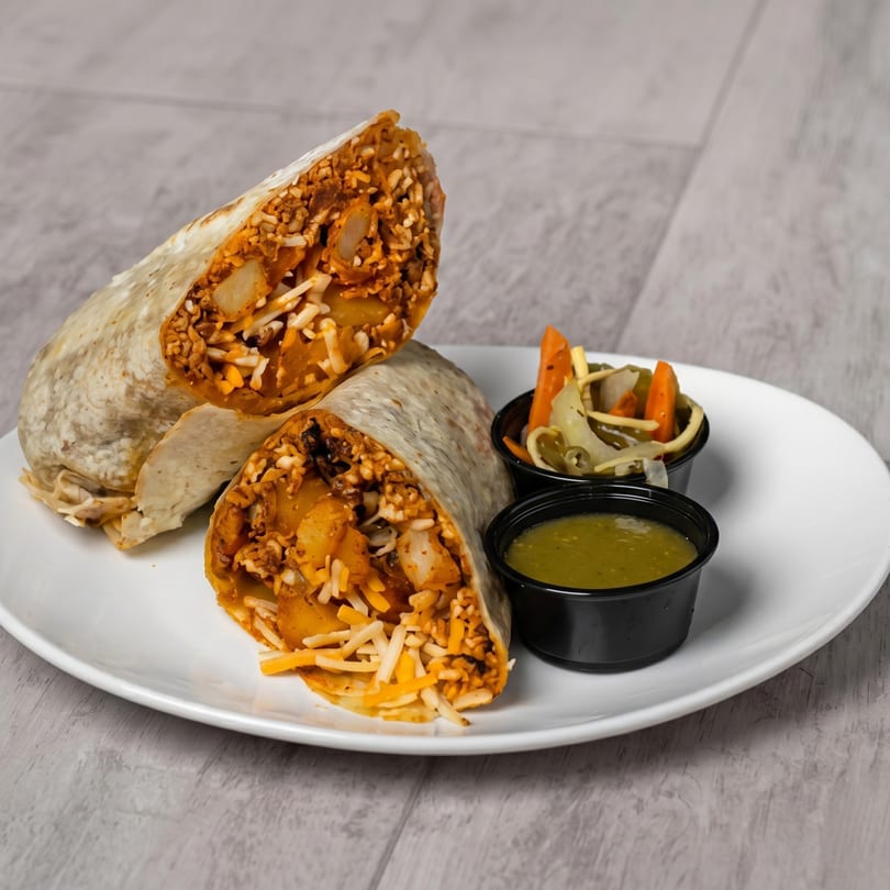 Two halves of a burrito filled with meat, rice, potatoes, and cheese, served with salsa and pickled vegetables.